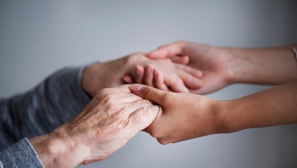Mani di un giovane appartenente al Volontariato di quartiere che aiuta un anziano